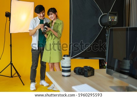 Lovely young asian female photographer showing a picture to a modeling man with  feeling very satisfied after taking his photograph with digital camera in a modern bright studio