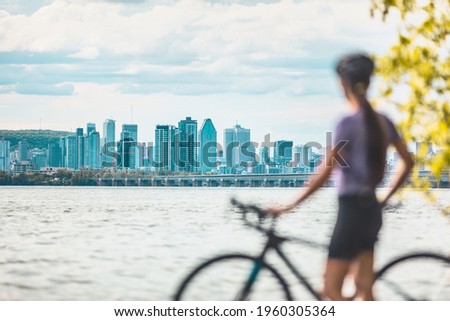 Montreal biking woman cyclist with bike looking at skyline view of condo towers and buildings downtown against Mount Royal landscape. Summer outdoor cycling sport active lifestyle.