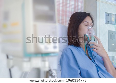 Sick beautiful female in blue cloth hold nasal mask with respiratory problem in hospital room. Asian woman patient inhalation therapy by the mask of inhaler with soft stream smoke from bronchodilator. Royalty-Free Stock Photo #1960334773