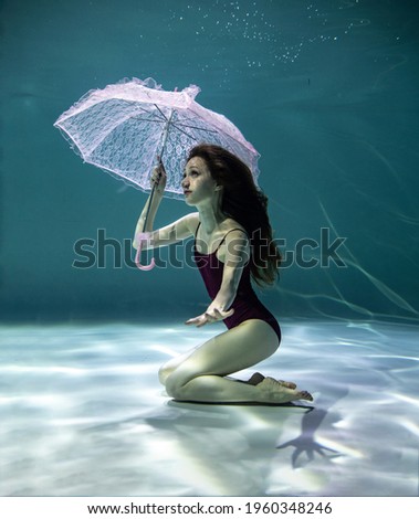 beautiful girl in a red swimsuit with a pink umbrella underwater on a blue background
