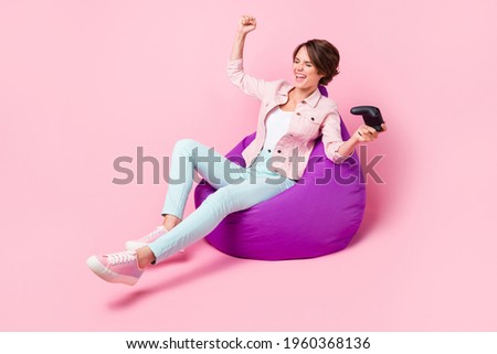 Full length profile side photo of cheerful victorious young girl sit bean bag hold joystick win isolated on pink color background