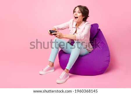 Full body profile side photo of excited young woman sit bean bag play game joystick look empty space isolated on pink color background