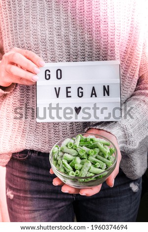 Lightbox with text GO VEGAN in female hands. Veganism, vegetarian healthy lifestyle. Frozen food in bowl. Healthy eating vegan. Green beans