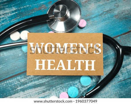 Text WOMEN'S HEALTH on a wooden blue background near a stethoscope and pills. Medical concept.