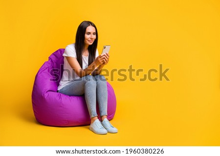 Full length body size photo brunette using smartphone app typing comment in soft chair isolated on vivid yellow color background