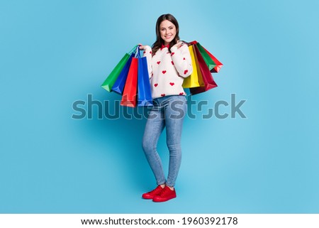 Full length photo of shiny cute young lady wear hearts print sweater holding colorful bargains isolated blue color background