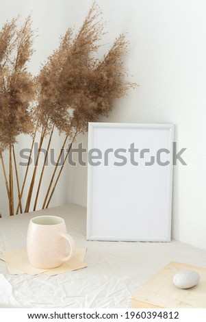 Home decor mock-up, blank picture frame near white painted concrete wall , dry Cane Reeds and old books, a cup of coffee