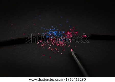 Black, colored pencils, on black background, and shavings from the pencils.