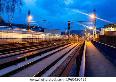 Railway at night on a river bridge in Hagen Hohenlimburg Germany with factories and industry. Long time exposure at evening blue hour in Germany. Passing Train in motion and flashing street lamps.