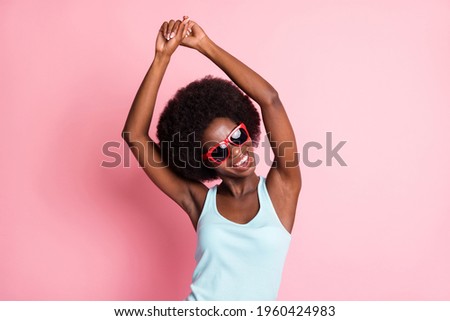 Portrait of optimistic brunette curly lady dance look empty space wear spectacles blue top isolated on pastel pink color background