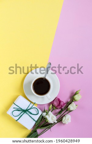 white cup with coffee and flowers and a gift on a yellow-pink background with a copy of the space, flat layout, top view.