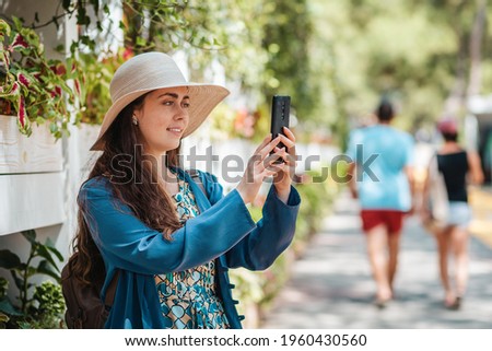 A happy woman in a hat takes photos and makes a video call via smartphone. Park street in the background. Concept of communication and social networks.