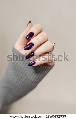 Female hand with long nails and dark purple lilac manicure holds a bottle of nail polish