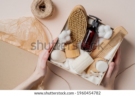 Beauty subscription Box preparation. Female hands holding gift box with natural skincare products, body brush, shampoo, soap, moisturizer. Royalty-Free Stock Photo #1960454782