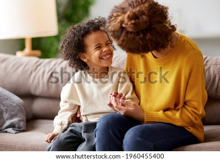 I love you, mom. Happy african american child son holding mothers hand, looking at her and smiling while sitting together on sofa in living room. Family mom and kid enjoying time together at home