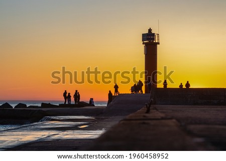Great view of the sea piers, lighthouses and dark silhouettes of holidaymakers watching and enjoying the bright orange sunset.Latvia, Mangalsalas pier. 