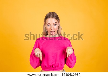 Pretty european woman in pink  blouse on yellow background happy excited cheerful point down with index finger