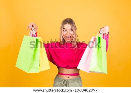 Pretty european woman in pink  blouse on yellow background holding shopping bags surprised shocked emotions, discount sale promotion concept cheerful happy