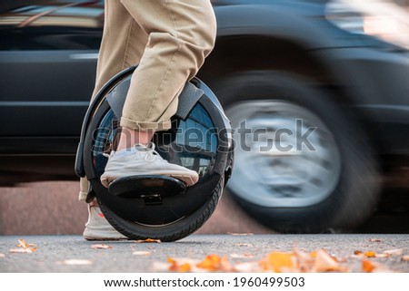 The legs of a young woman ready to ride an electric unicycle, abbreviated EUC, against the background of evening or morning city traffic. An unrecognizable woman on an electric monowheel. Royalty-Free Stock Photo #1960499503