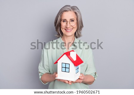 Photo of lovely smiling good mood granny in glasses hold little house moving relocation isolated on grey color background