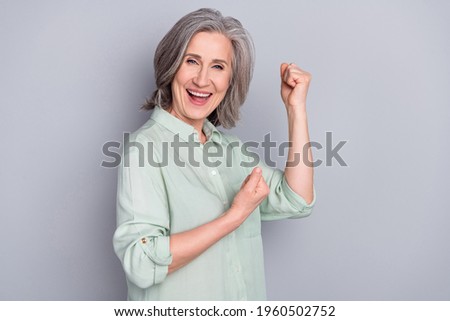 Photo of mature smiling good mood excited woman raise fists in victory success triumph isolated on grey color background