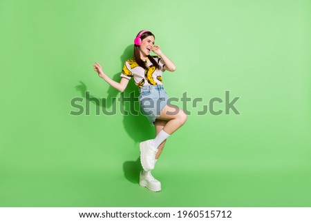 Full body photo of joyful happy cheerful girl look empty space wear headphones isolated on green color background