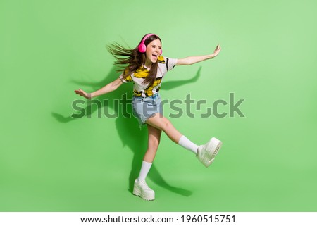 Full body photo of brunette dreamy young woman look empty space hands wings dance wear headphones isolated on green color background Royalty-Free Stock Photo #1960515751