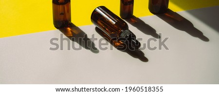 A set of bottles for cosmetic products on a yellow-white background. The containers are standing, and the shadow falls on the background. One bottle lies on the surface. Hard light. Banner