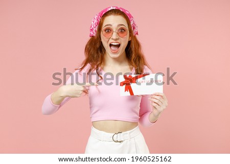 Young surprised cheerful happy woman wear rose clothes bandana glasses point index finger on gift voucher flyer mock up isolated on pastel pink background studio portrait. People lifestyle concept.