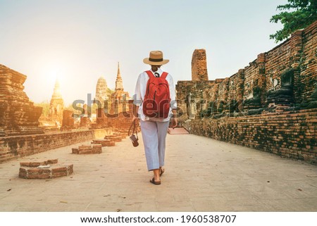 Young woman tourist walking with compact photo camera through Ayutthaya Wat Phra Ram ancient ruins in Thailand. History, tourism, sightseeing concept.