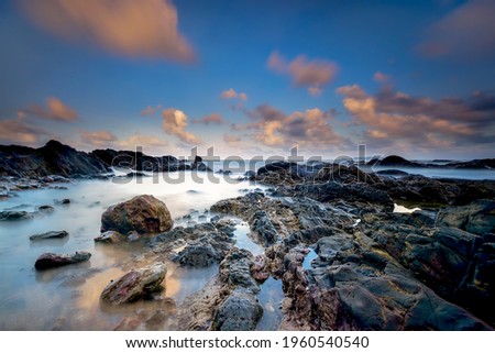 rocky beach with wonderful sunrise , located at Terengganu, Malaysia. long exposure photography. soft and grain image.