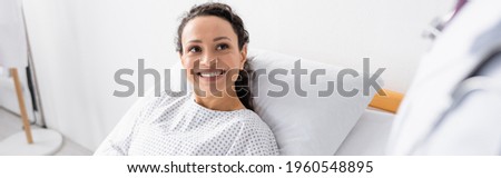 cheerful african american woman smiling near doctor on blurred foreground, banner Royalty-Free Stock Photo #1960548895