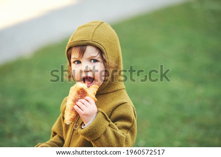 Outdoor portrait of cute 1 - 2 year old toddler kid eating croissant