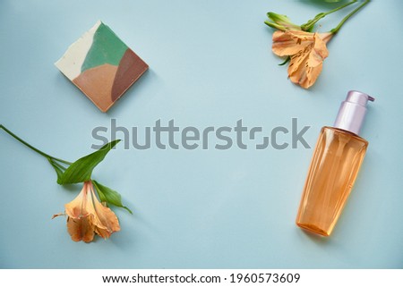 Female background concept on blue background. Cosmetic products and flowers. Mock up bottle