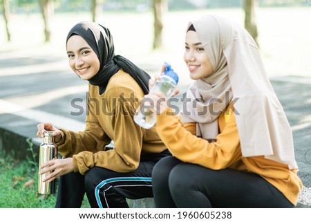 two veiled girls sitting enjoy drinking water with bottle after doing outdoor sports together the garden field