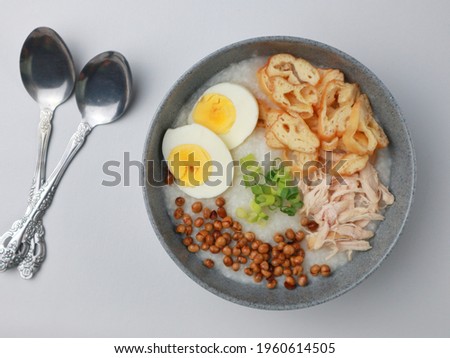 Bubur ayam Bandung or Chicken Porridge, Indonesian traditional food consist of white rice porridge, shredded chicken, cakwe, fried soybean, crackers, leek and egg. Selective focus.  Royalty-Free Stock Photo #1960614505
