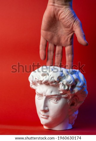 Plaster pot in the form of David's head and male hand on a red background.