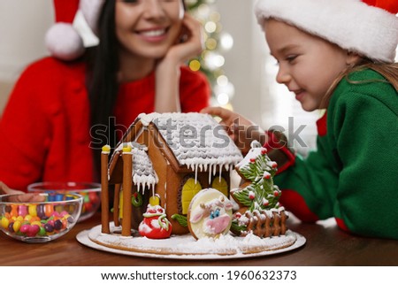 Mother and daughter with gingerbread house at table indoors, closeup