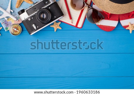 Overhead photo of camera notebook pencil compass hat sunglasses sandals map starfishes and airplane isolated on the blue background with empty space