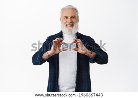 Smiling senior man with tattoos showing credit card, recommending his bank, pleased with service, standing over white background