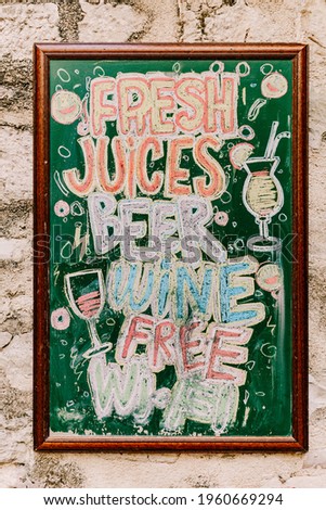 Wooden easel drawn with multicolored crayons hangs on the stone wall of the building. Title: Fresh juices beer wine free wi-fi