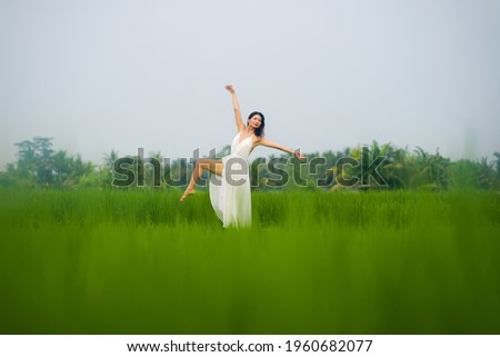 artistic portrait of young attractive and happy Asian woman outdoors at green rice field landscape wearing elegant long dress dancing on beautiful nature carefree 