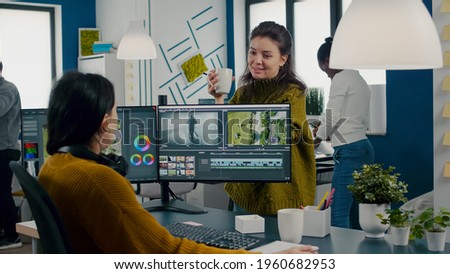 Team of videographers talking about project while working in video editing app at computer with dual monitors setup sitting in modern digital multimedia company. Creatice women prosessing film montage