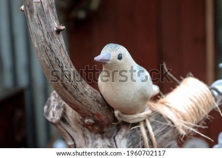 Fake clay bird sitting on old tree branch without bark. Black eyes, purple beak