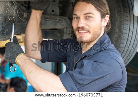 The mechanic is smiling happily at work. Mechanic reparing the car in the workshop garage. Auto mechanic hands using wrench to repair a car engine. 