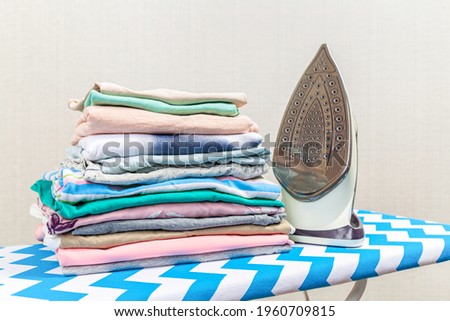 Folded ironed men's shirts lie next to the iron on the ironing board.