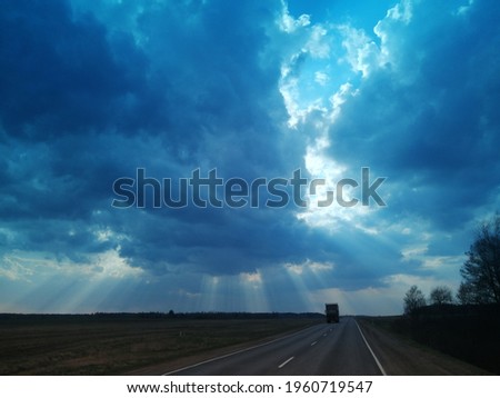 Sunbeams piercing through the clouds over the field and the road, sky burst, blue filter