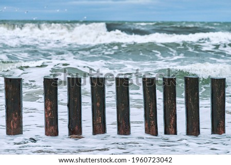 High wooden breakwaters in splashing sea waves, beautiful cloudy sky, close up view. Long poles or groynes in stormy sea.
