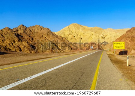 View of desert road 12, with a trilingual warning sign (dangerous curves) and landscape. Eilat mountains, southern Israel