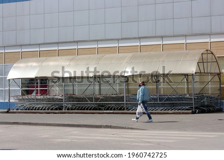 A man in a blue jacket with a white package walks near the storage area of the shopping carts